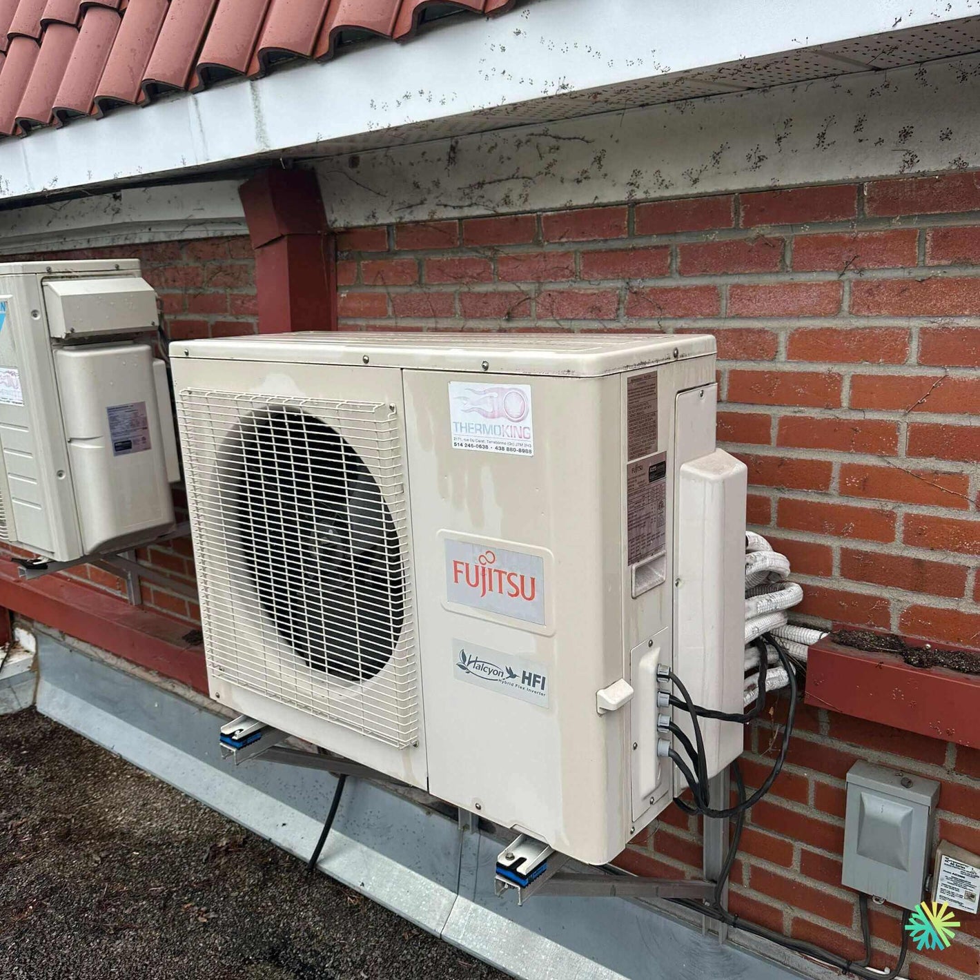 Outdoor Fujitsu air conditioning unit mounted on a brick wall under a tiled roof.