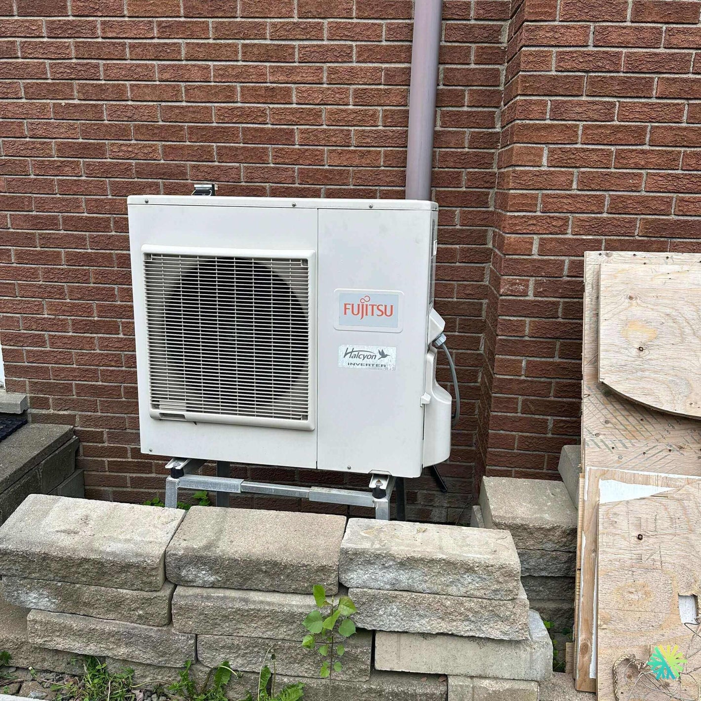 Fujitsu outdoor air conditioning unit installed on a brick wall with stacked stones in the foreground.