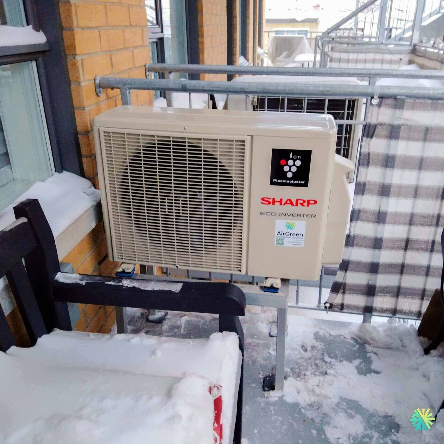 Outdoor Sharp air conditioner unit with eco inverter technology installed on a snowy balcony.