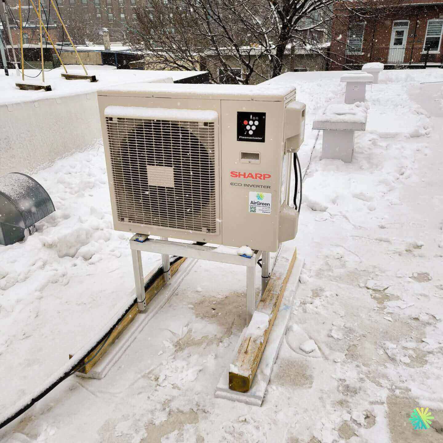 Sharp eco inverter air conditioner unit installed on a snowy rooftop in winter setting under cloudy skies.