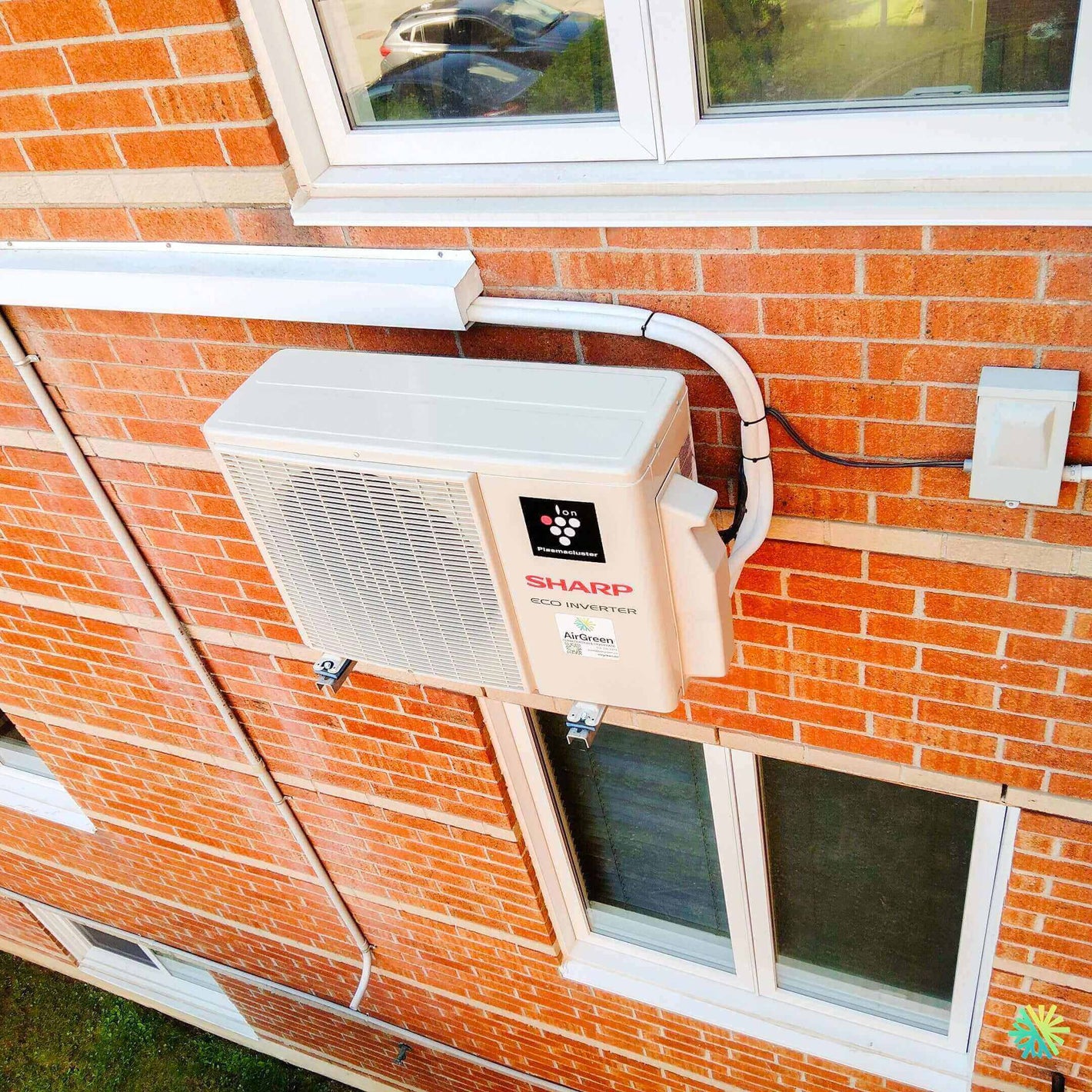 Outdoor Sharp air conditioning unit installed on red brick wall of a building.