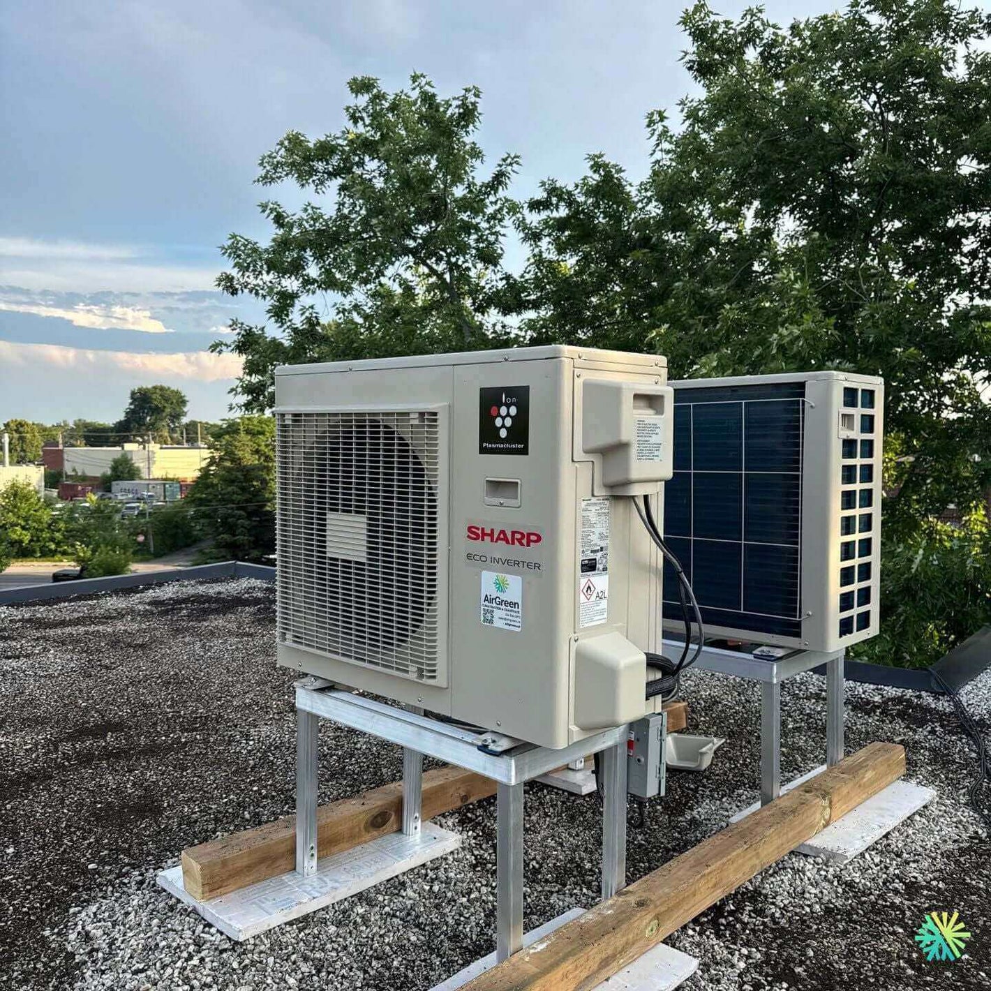 Rooftop view of a Sharp eco inverter air conditioning unit under a clear sky, surrounded by greenery.