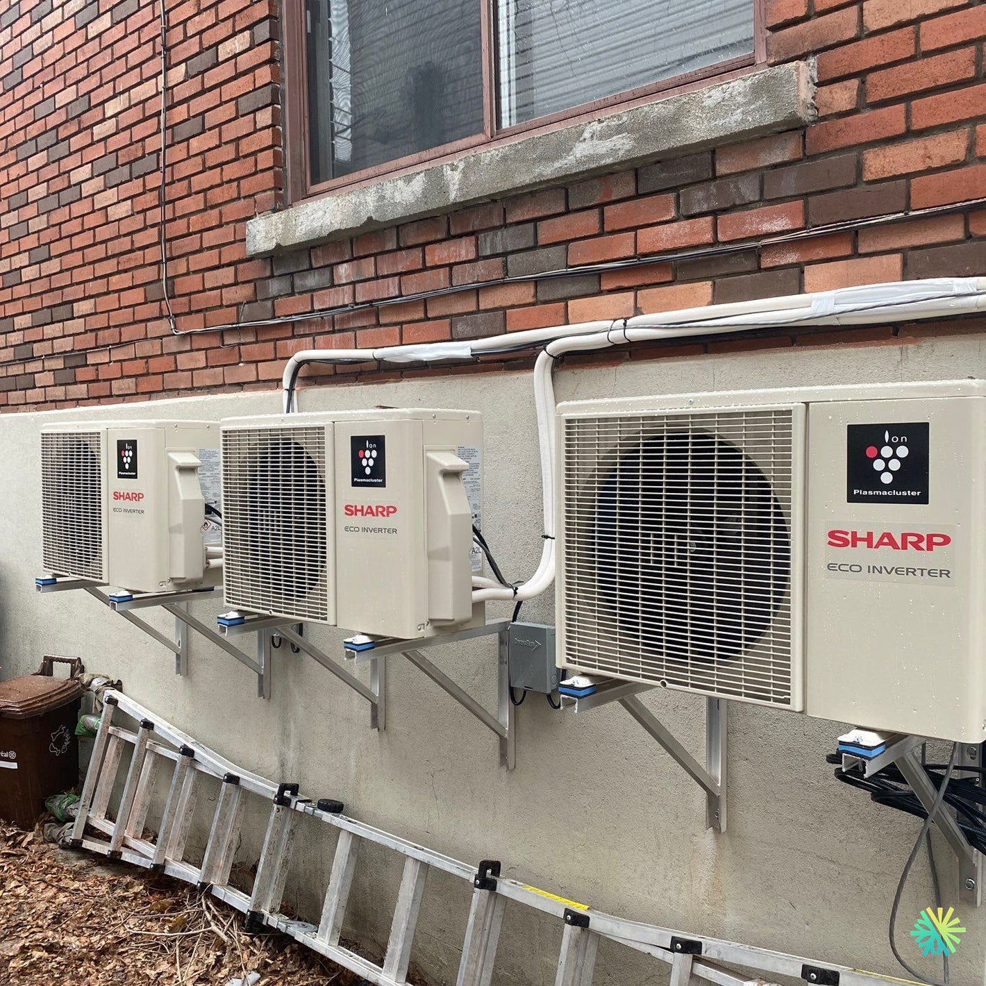 Sharp Eco Inverter air conditioning units mounted on exterior brick wall next to window, installation site view.