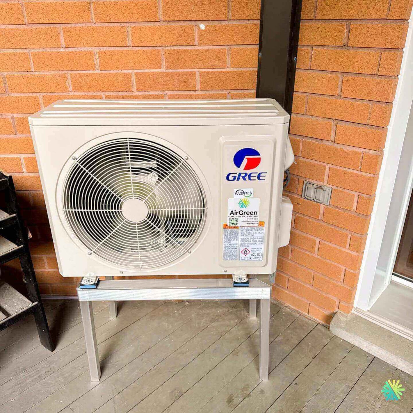 Outdoor Gree air conditioner unit mounted on a stand against a brick wall.