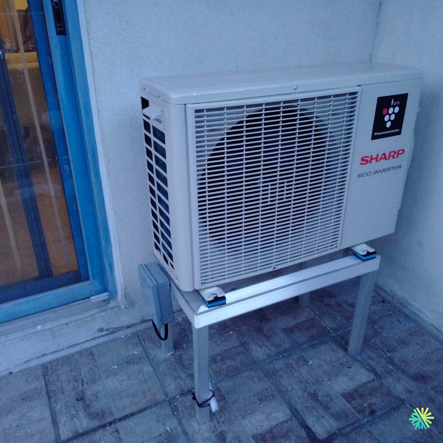 Air conditioning unit installed outdoors featuring Sharp Eco Inverter technology on a metal stand.