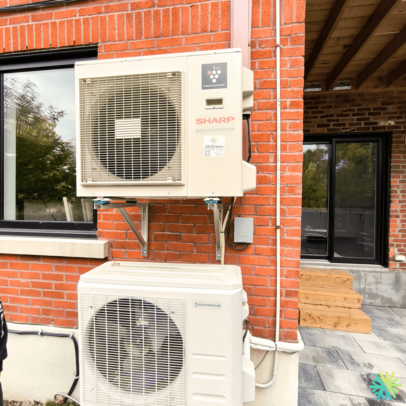 Two outdoor air conditioning units mounted on a brick wall beside a modern glass door, showcasing energy-efficient home cooling solutions.