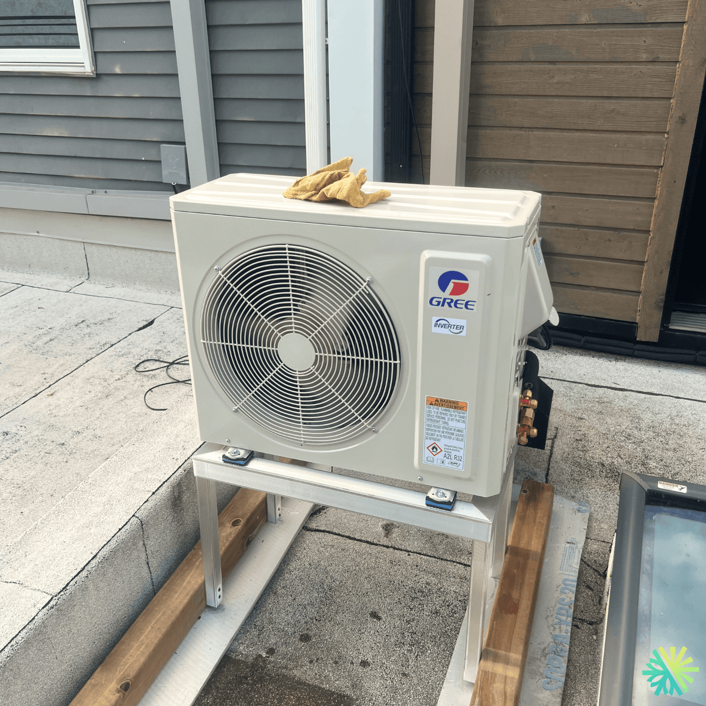 Outdoor Gree AC unit installed on a rooftop platform with yellow gloves on top, showcasing residential air conditioning equipment.