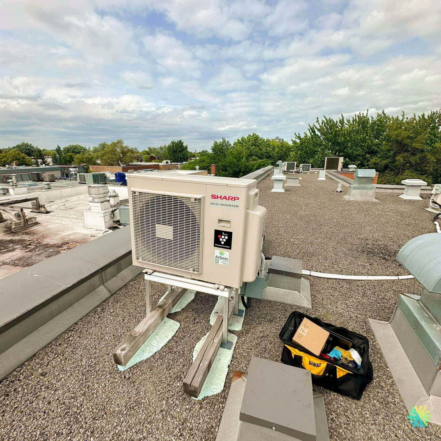 Residential rooftop HVAC system with Sharp branding, surrounded by trees and a cloudy sky.
