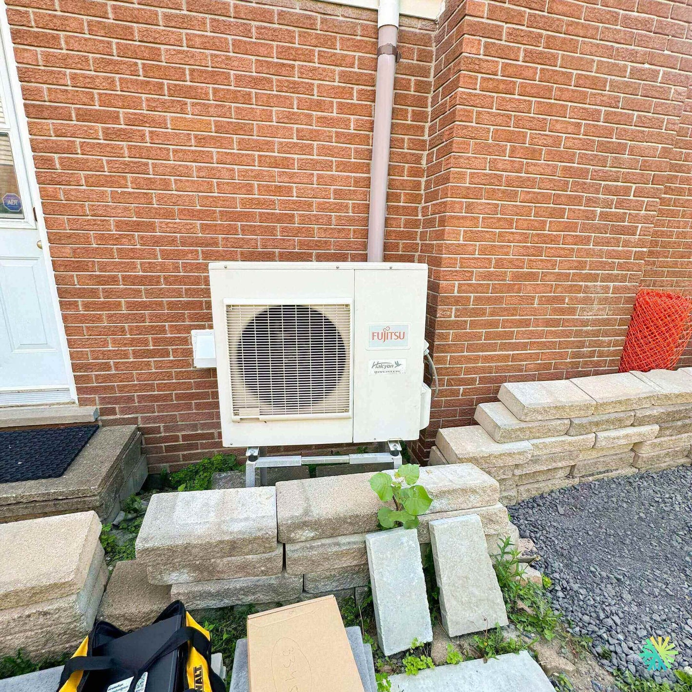 Outdoor Fujitsu air conditioning unit mounted on a brick wall with concrete blocks at the base.