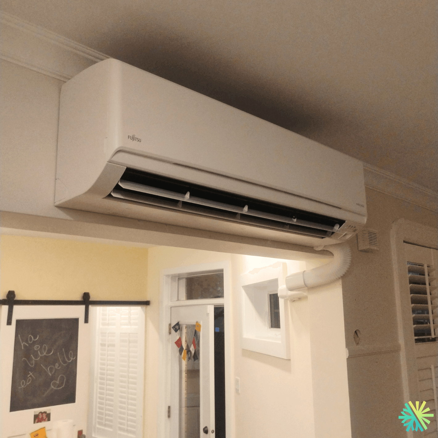 Wall-mounted Fujitsu air conditioner in a modern room with chalkboard door and window, featuring sleek design and efficient cooling.
