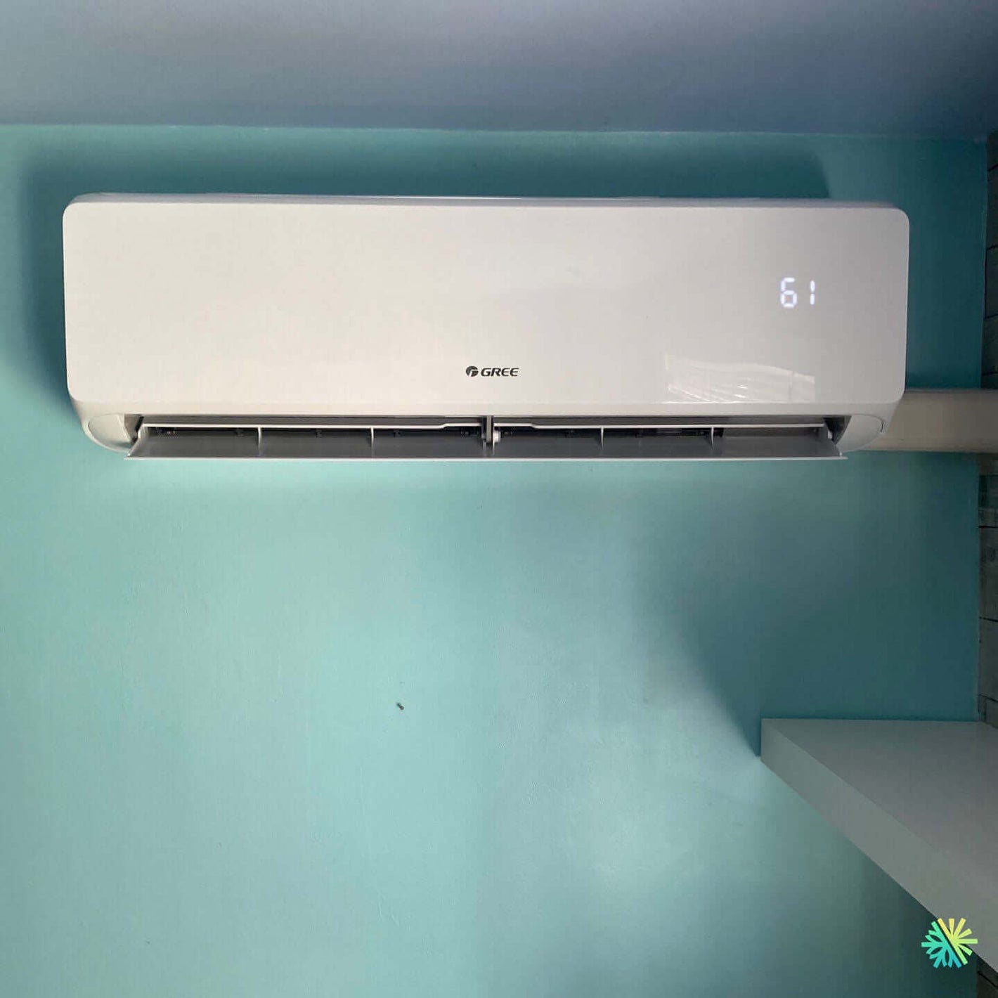 Wall-mounted Gree air conditioner in operation, set at 61 degrees, against a blue wall. Energy-efficient cooling solution.