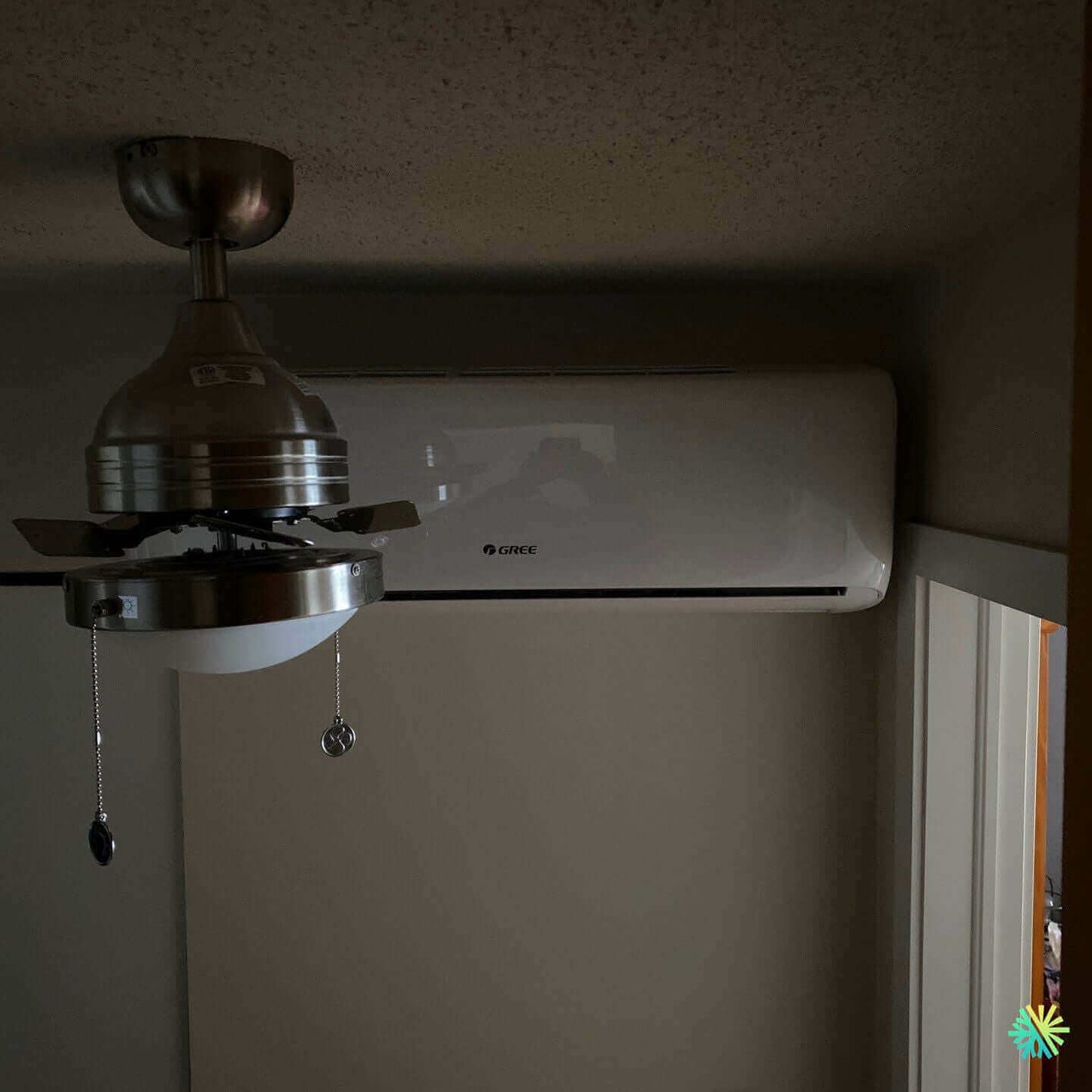 Ceiling fan and Gree air conditioning unit installed in a room corner for climate control.