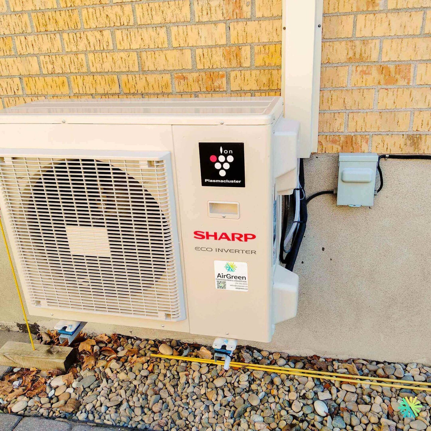 Sharp Eco Inverter air conditioning unit installed outside a brick building on a rocky surface.