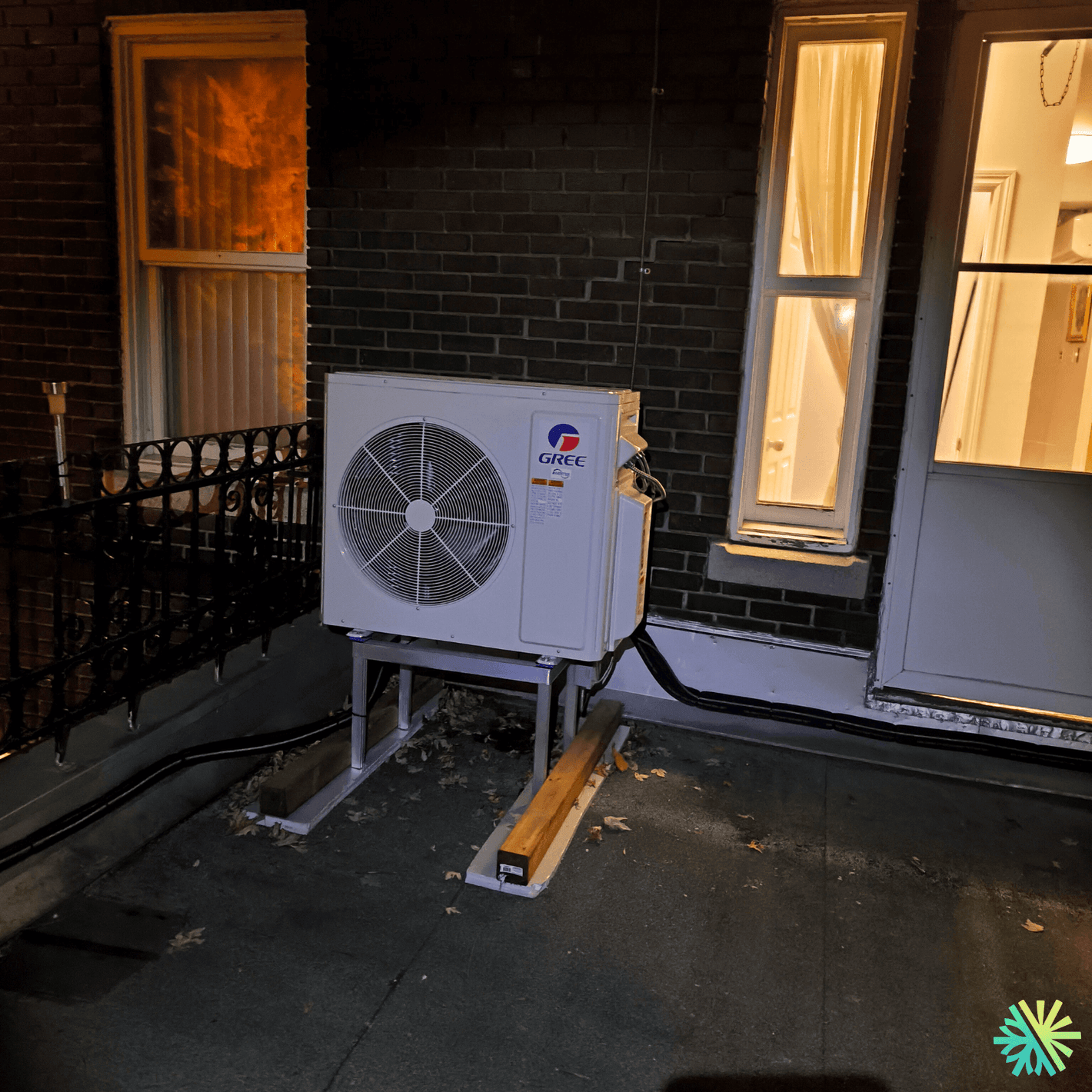 Outdoor Gree air conditioning unit installed on balcony at night, near brick wall and windows.