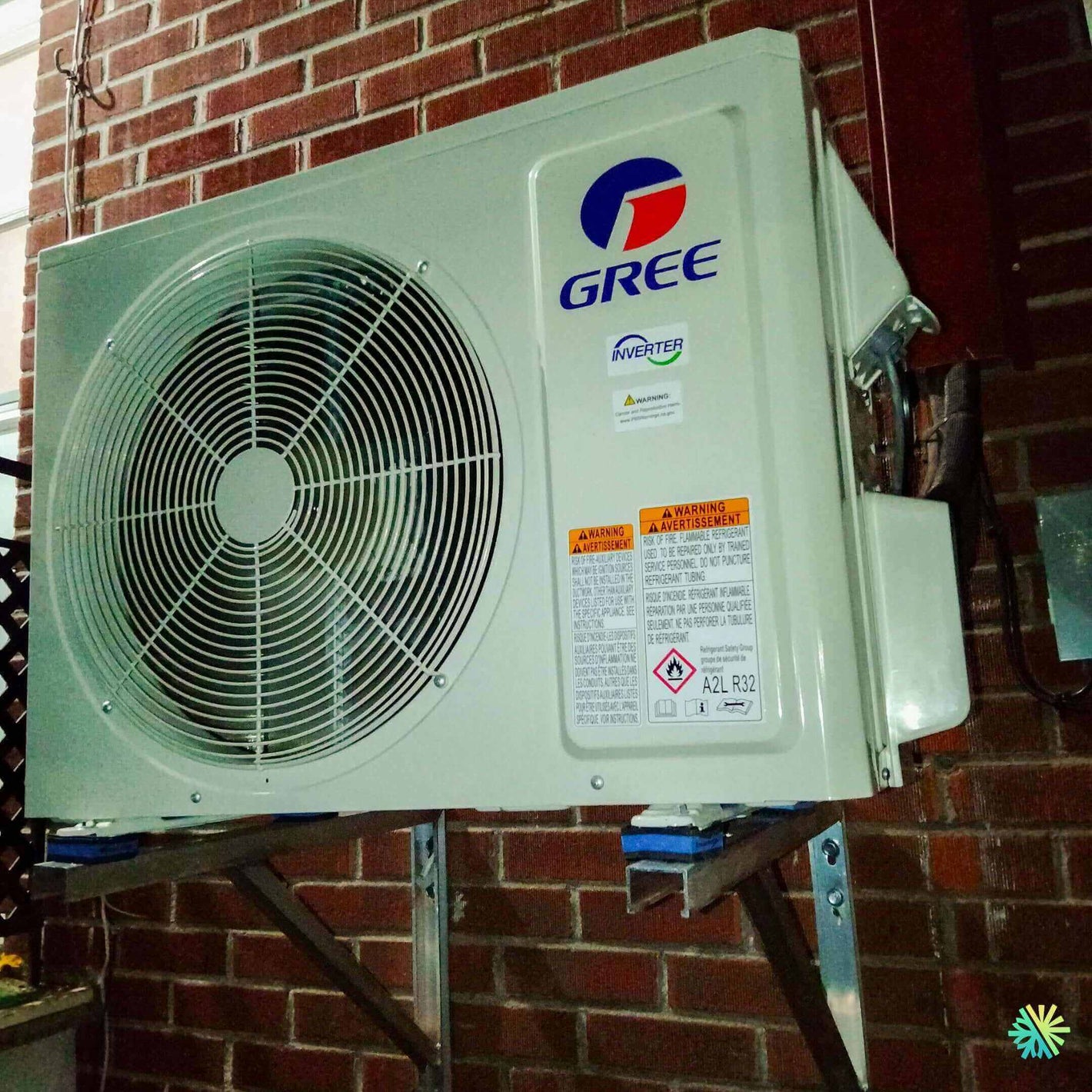 Outdoor Gree inverter air conditioning unit mounted on brick wall, showing fan and warning labels