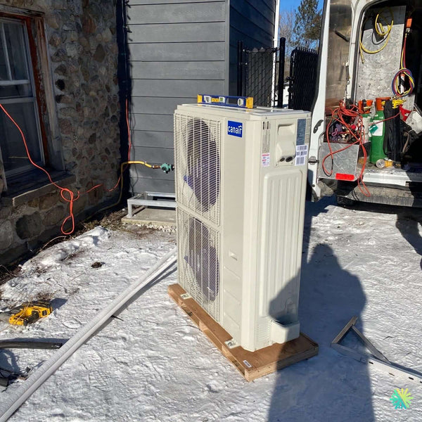 Outdoor air conditioner unit installation next to a stone wall on a snowy day, with some electrical tools and wires visible in the scene.