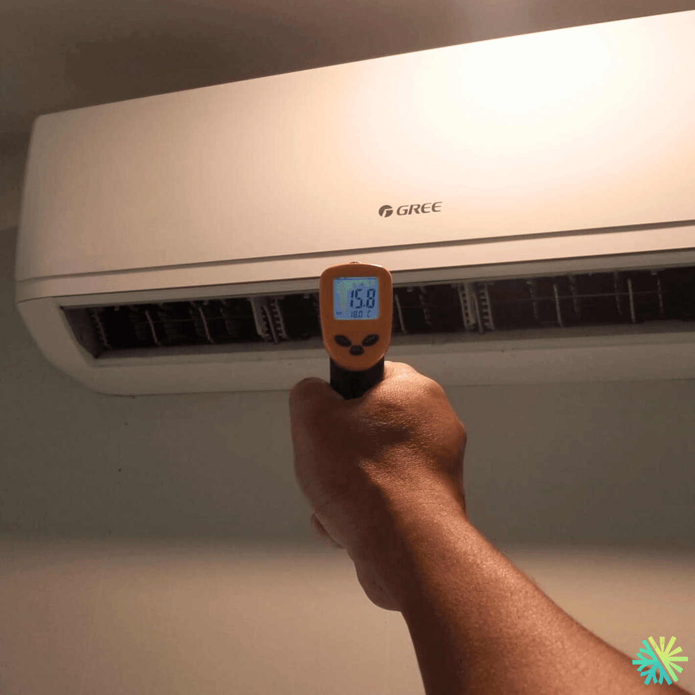 Hand holding infrared thermometer measuring temperature of air conditioner unit