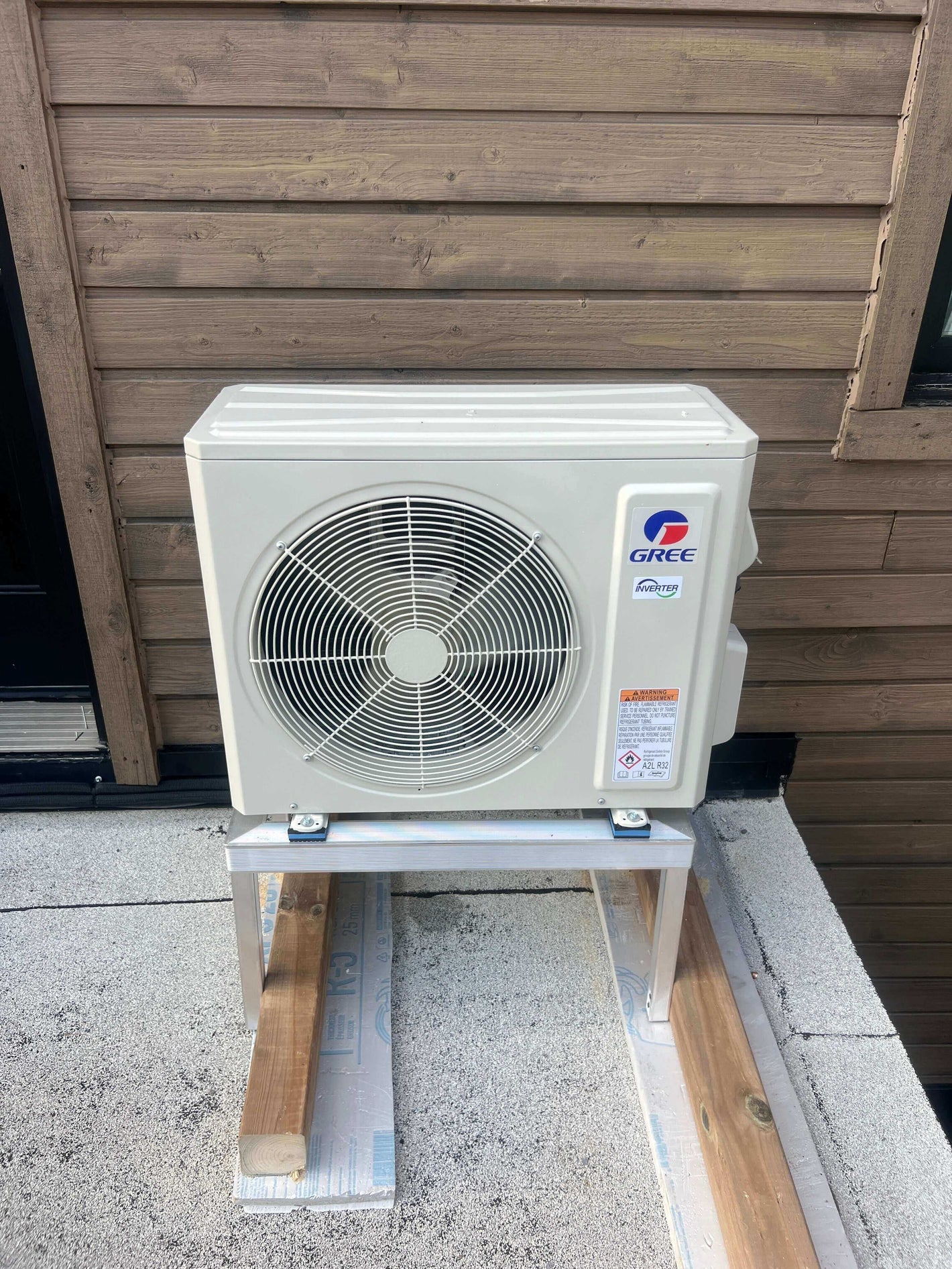 Outdoor Gree AC unit installed on a wooden platform near a wall, emphasizing energy-efficient cooling.