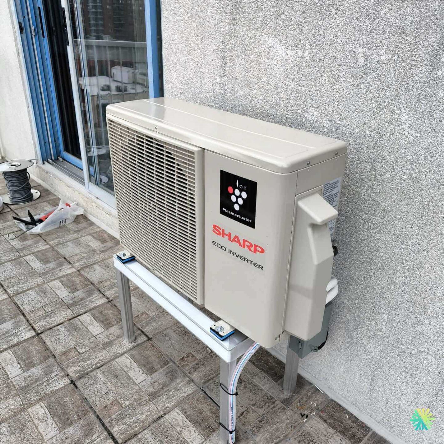 Sharp Eco Inverter outdoor air conditioning unit installed on a tiled balcony near a glass window.