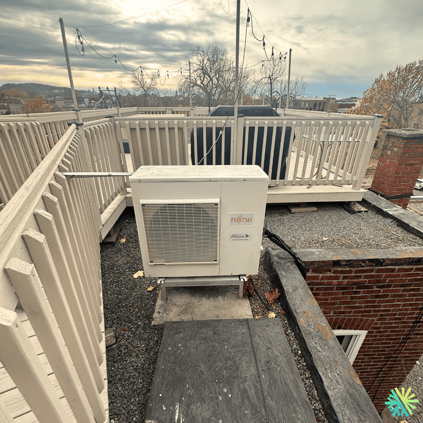 Outdoor Fujitsu air conditioning unit installed on a rooftop deck with railings, sky view, and cityscape in the background.