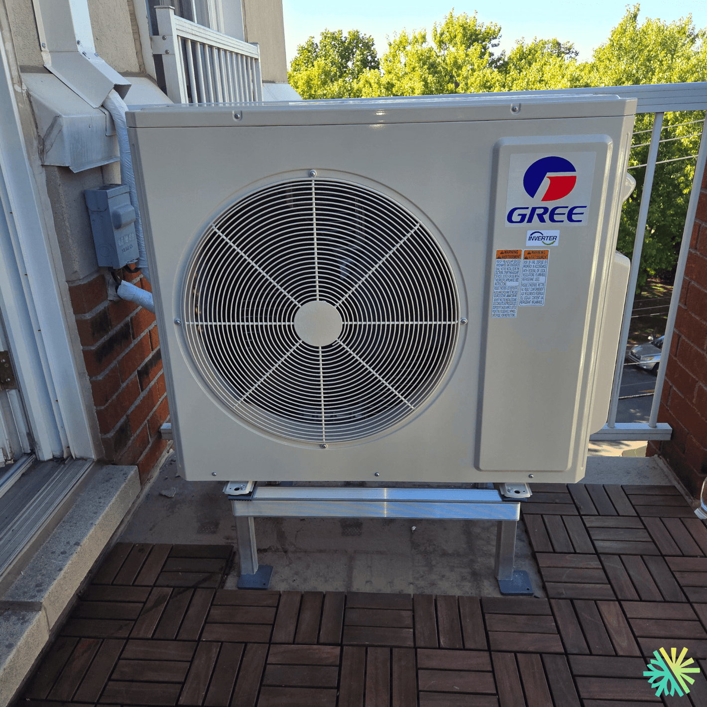 Outdoor Gree air conditioning unit installed on a balcony, surrounded by greenery and patio flooring.