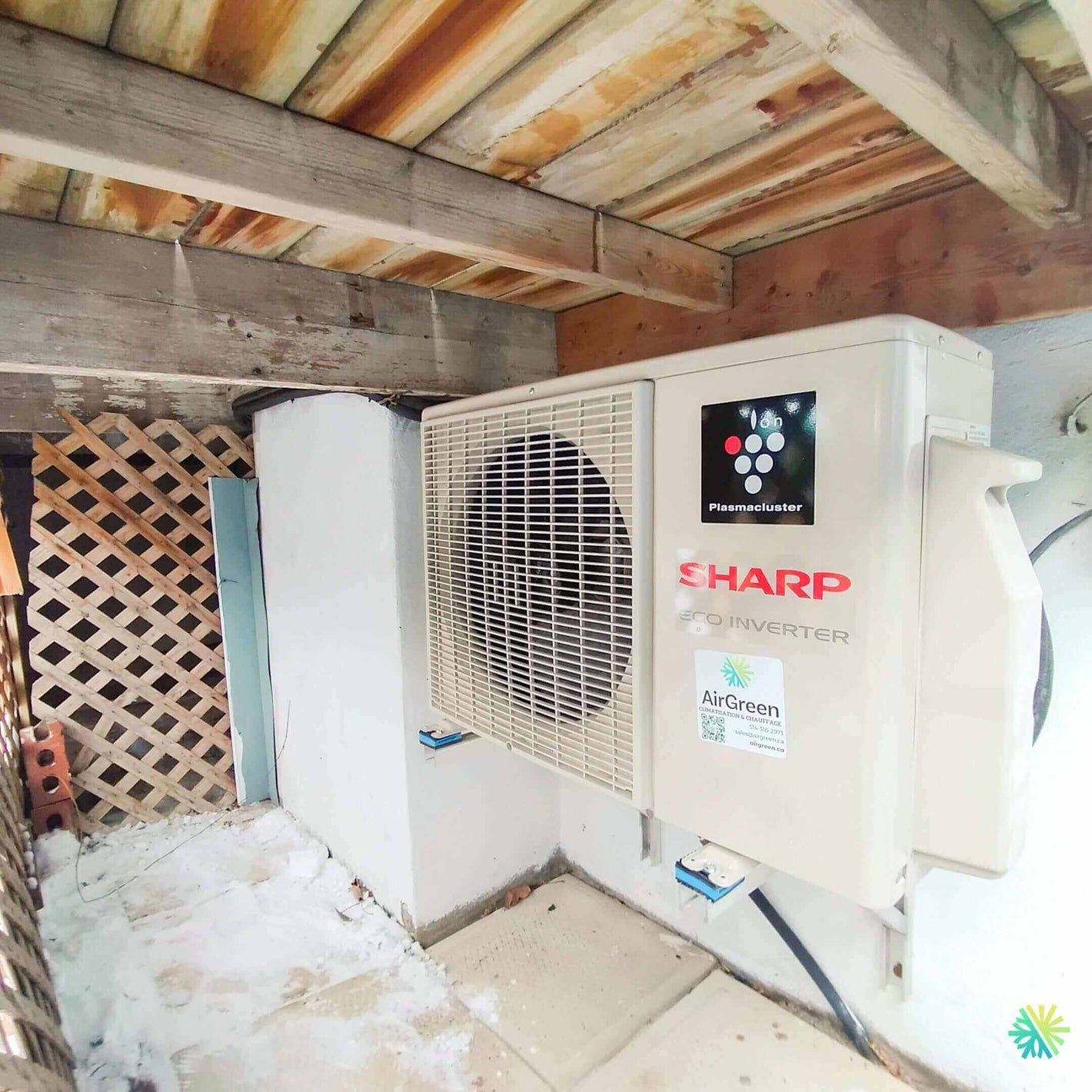 Sharp air conditioner unit installed under wooden deck with snow around
