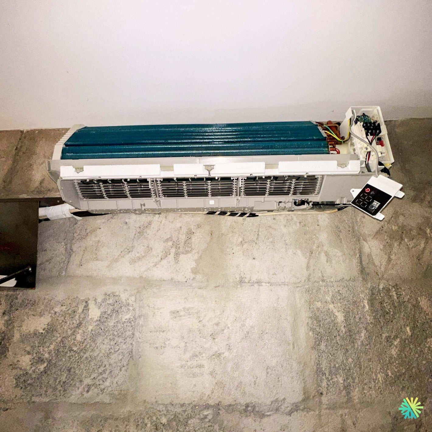 Disassembled air conditioner unit on stone floor for repair, showcasing internal components and wiring.