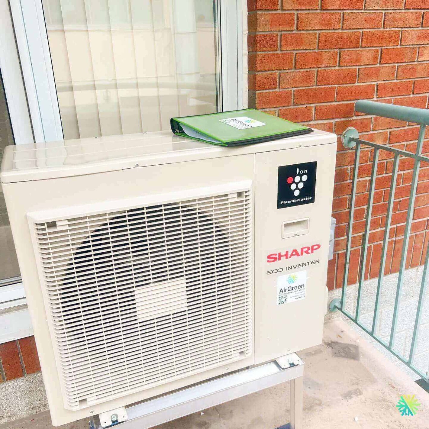 Sharp Eco Inverter air conditioning unit installed outdoors on a balcony near a red brick wall and window.