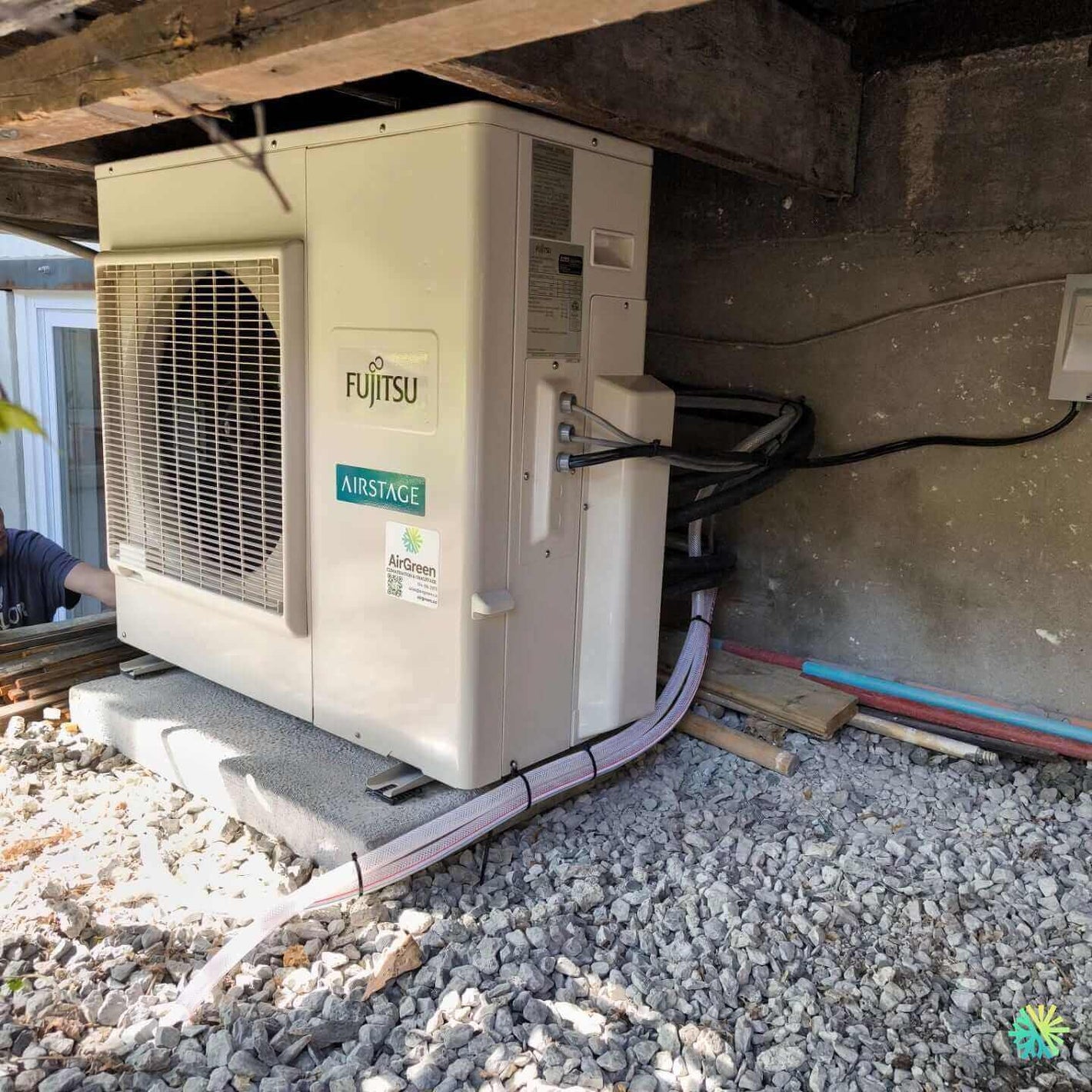 Fujitsu Airstage outdoor unit installed under a house with exposed cables on a gravel bed.