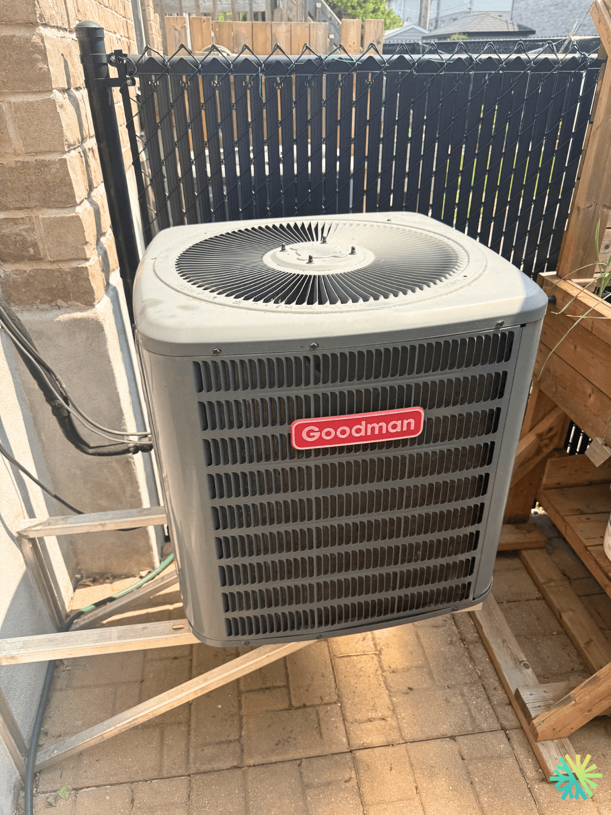 Outdoor Goodman air conditioning unit next to a brick wall and black fence on a patio