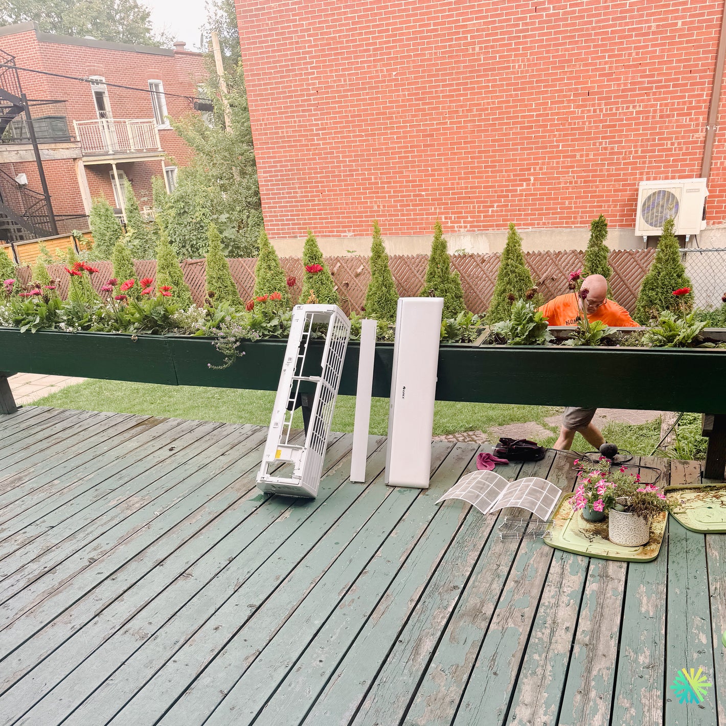 Person installing air conditioner unit amidst rooftop garden setting with tools and plant arrangement visible.