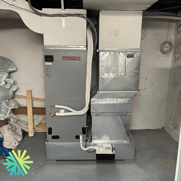 Basement HVAC unit installation in a utility room corner with pipes and ventilation ducts.