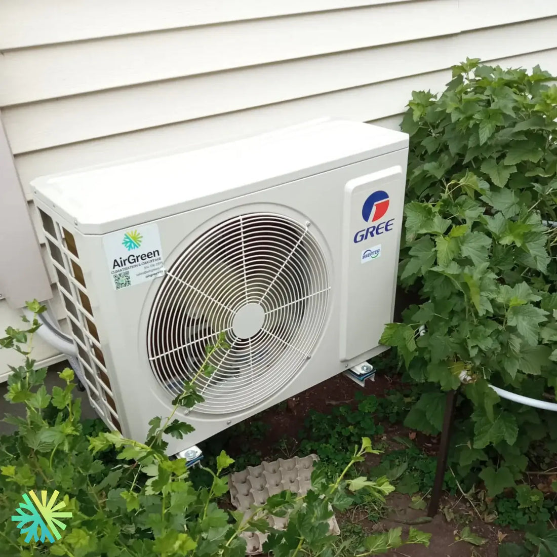 Outdoor GREE AirGreen unit installed next to a house, surrounded by green shrubs.
