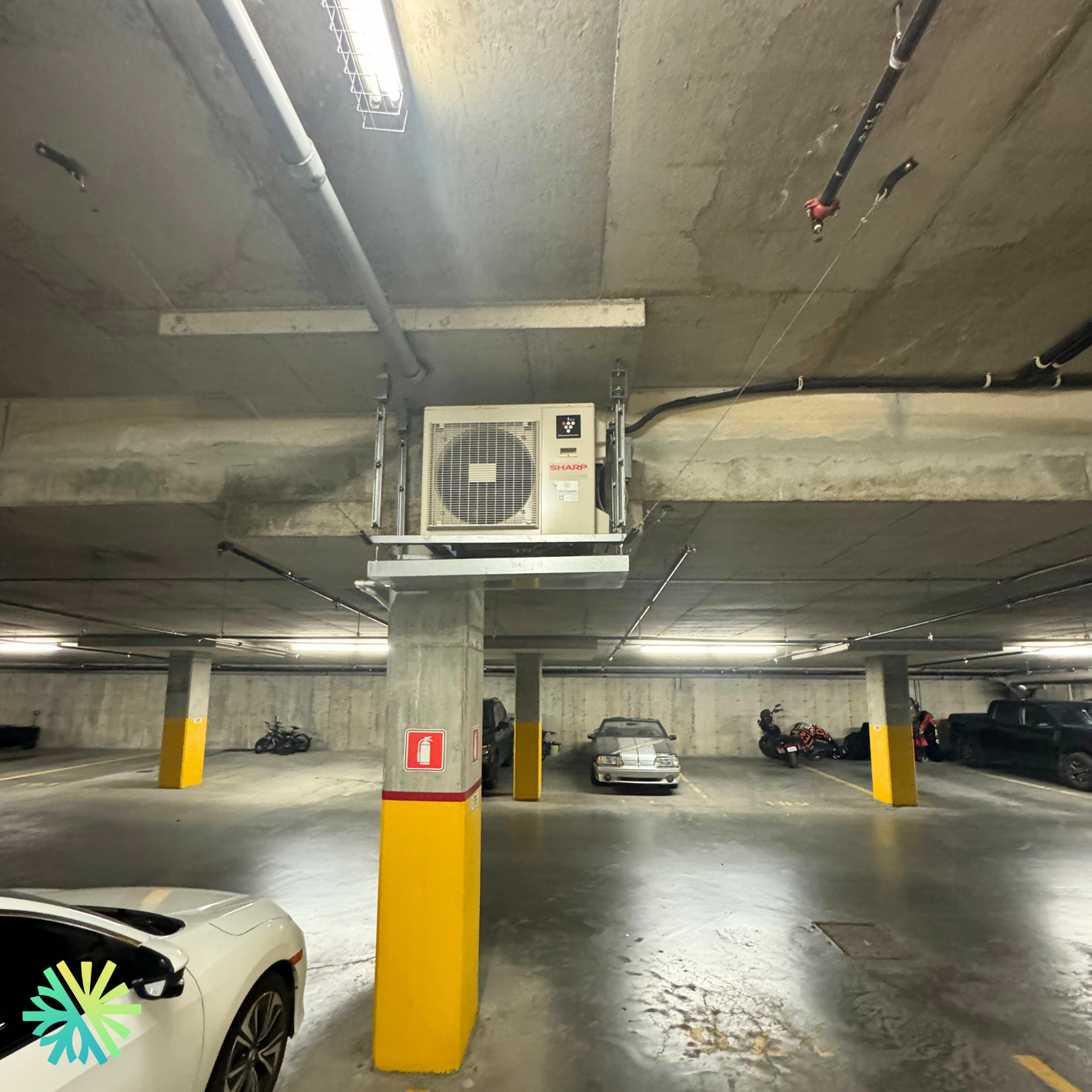 Indoor parking garage with air conditioning unit installed on a concrete column. Cars parked around the area.
