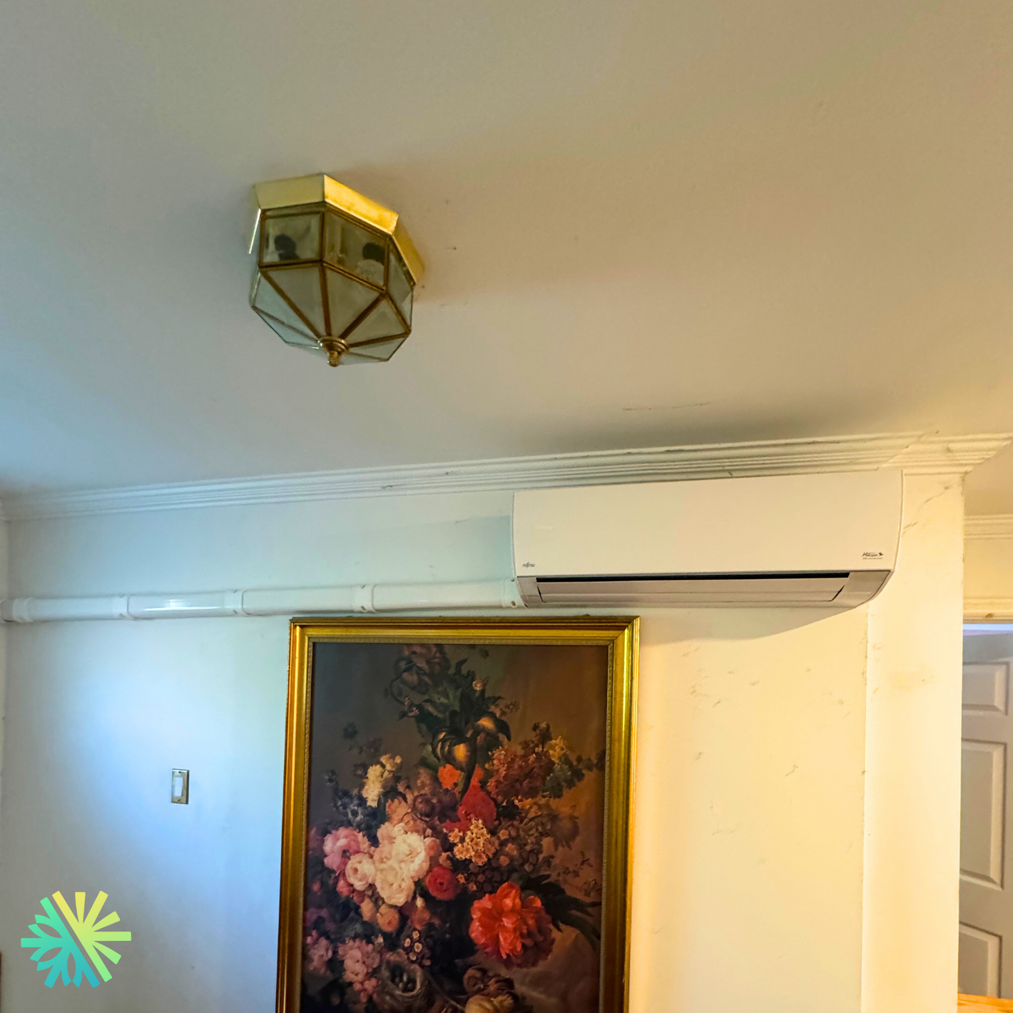 Stylish room with geometric ceiling light, air conditioner, and floral painting.
