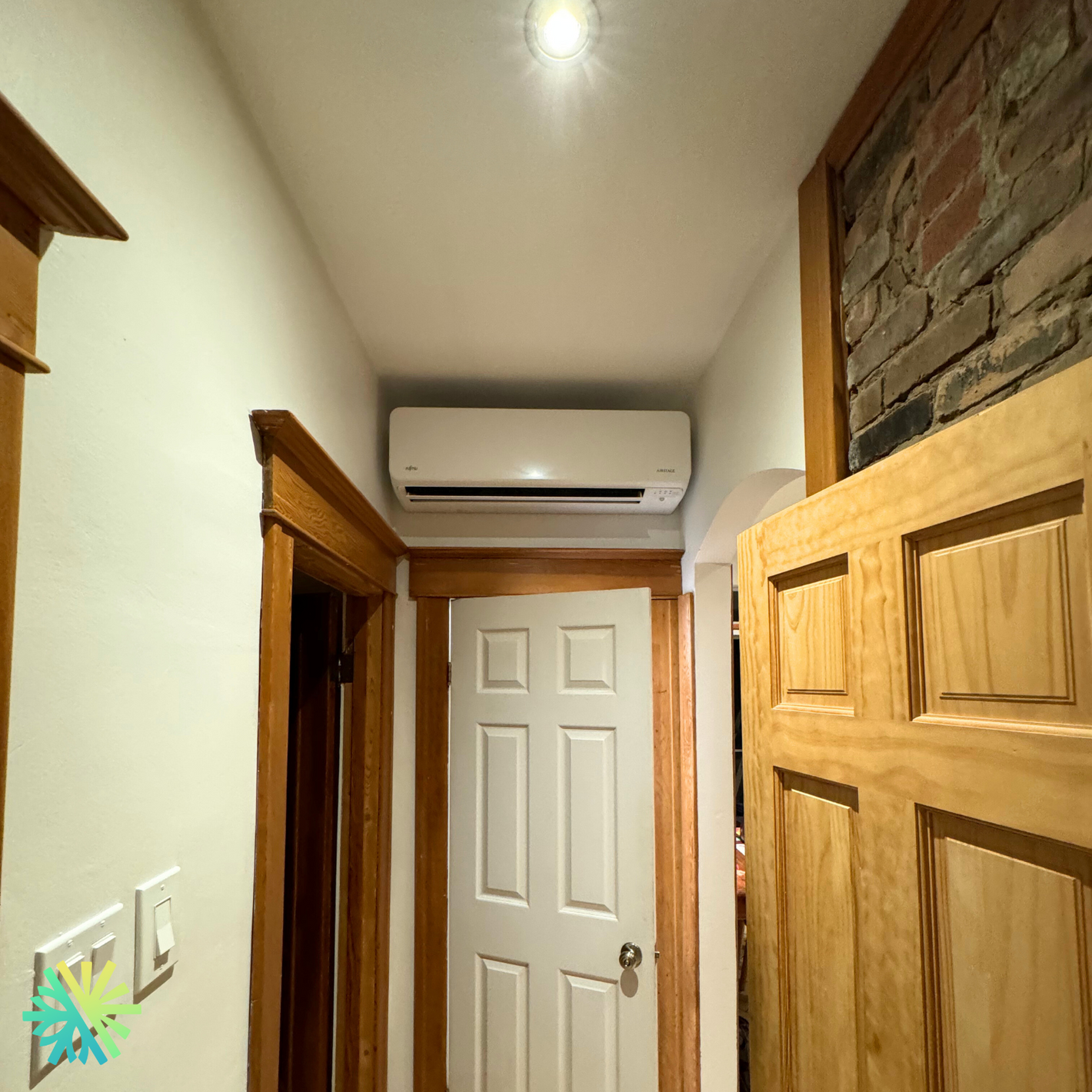 Modern air conditioning unit installed above a wooden doorway in a cozy interior hallway with warm lighting.
