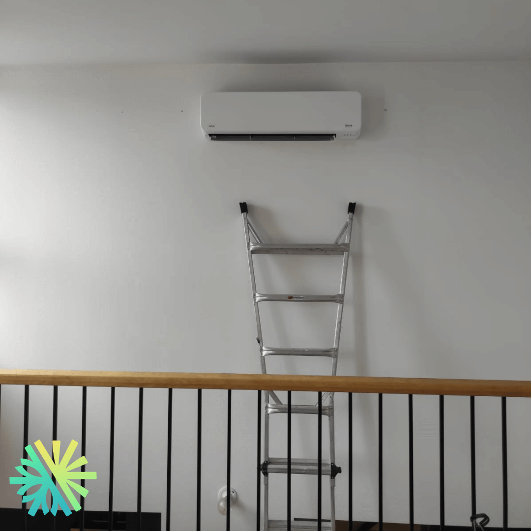 Air conditioner installed high on a wall above a metal ladder, indoors.